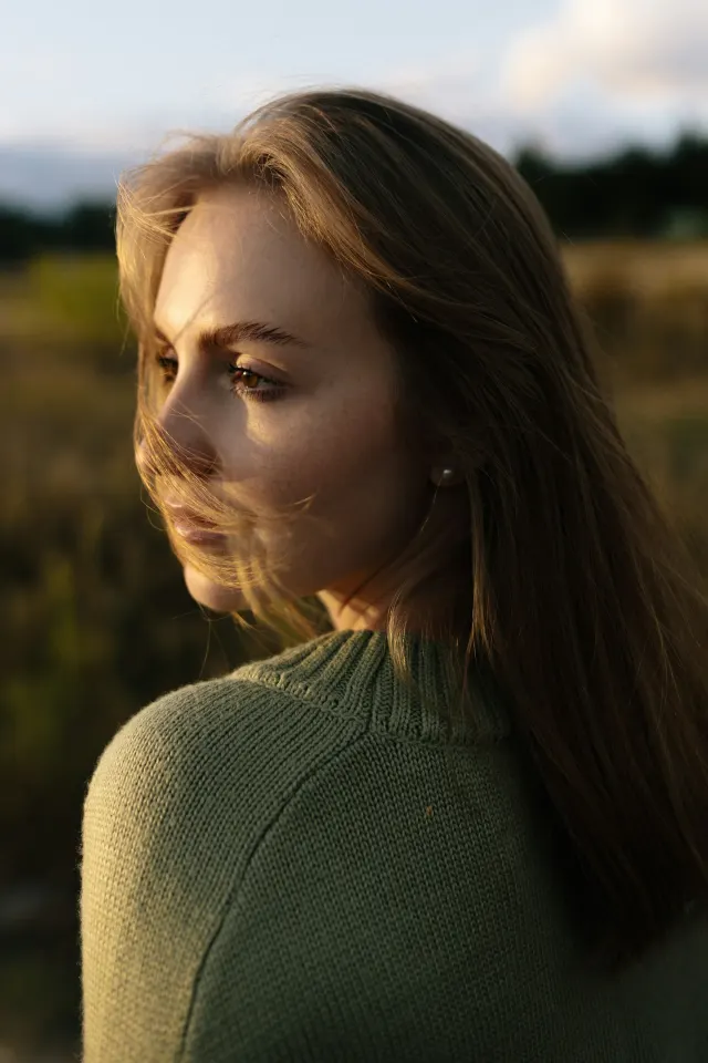 A woman in a green jumper in profile, in low golden light